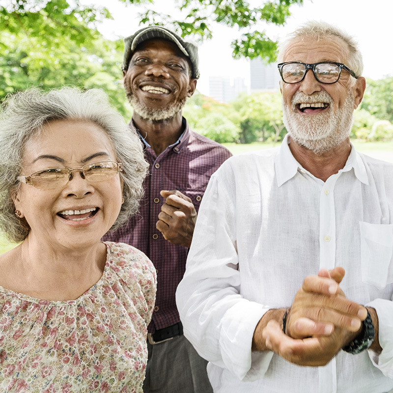 Three seniors laughing together outside under a tree.